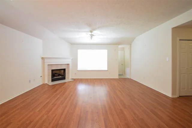 an empty room with wooden floor fireplace and windows
