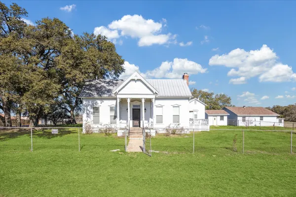 a view of a white house in a big yard with palm trees