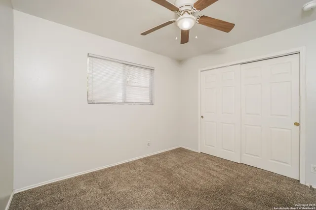 an empty room with a chandelier fan and windows