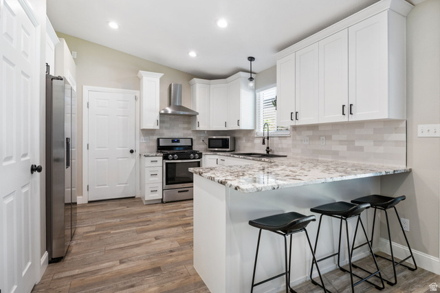 415 360 East Salem, UT 84653 - Photo 3 of 20 Kitchen featuring white cabinetry, stainless steel appliances, speckled countertops, a tile backsplash, and wood-finish flooring