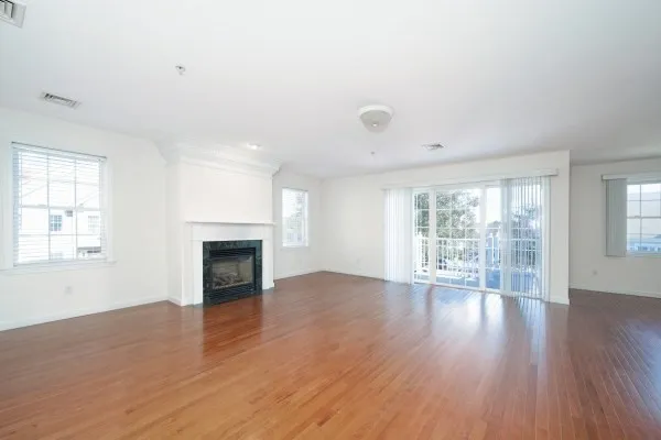 an empty room with wooden floor fireplace and windows