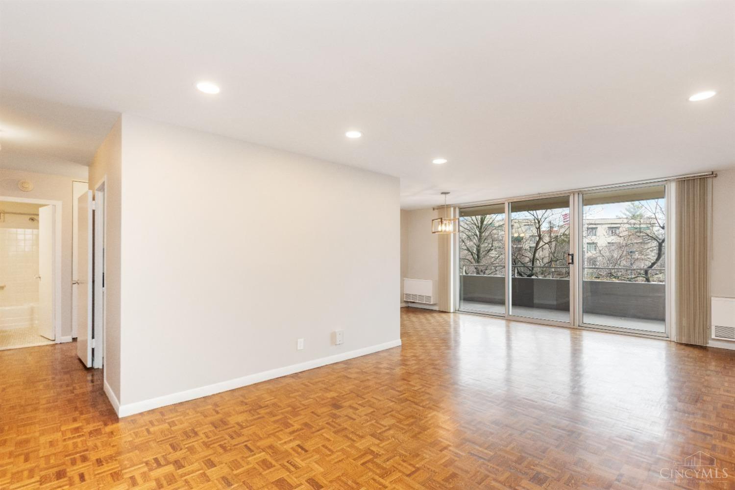2324 Madison Road, Unit 204 Cincinnati, OH 45208 - Photo 11 of 34 Living room/dining room combo features beautiful hardwood floors and is flooded with natural light from the wall of windows that lead to the covered open-air balcony. The trees while in bloom provide privacy as well as a serene feel of nature.