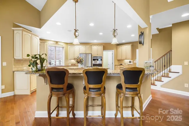 a kitchen with stainless steel appliances granite countertop a refrigerator a sink dishwasher a stove and white cabinets with wooden floor