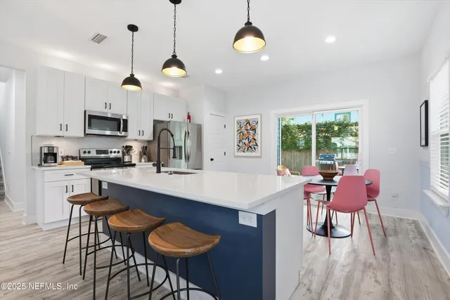 a kitchen with stainless steel appliances kitchen island granite countertop a sink a stove a dining table and chairs with wooden floor