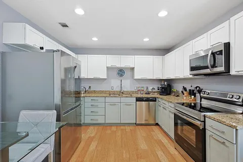 a kitchen with stainless steel appliances granite countertop a stove top oven a sink dishwasher a refrigerator and white cabinets with wooden floor