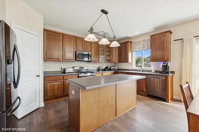 a kitchen with stainless steel appliances granite countertop a refrigerator a sink dishwasher a stove top oven a kitchen island and chairs with wooden floor