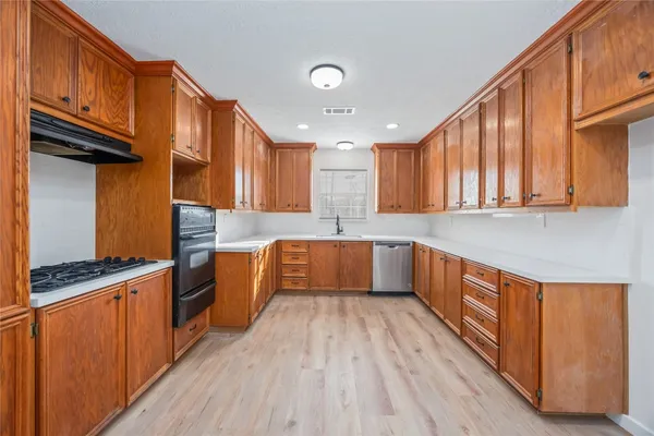 a kitchen with stainless steel appliances a sink dishwasher a stove top oven a refrigerator with wooden cabinets and floor