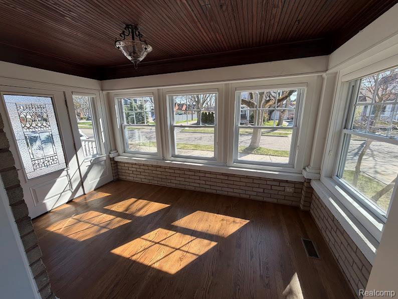 Unfurnished sunroom with wood finished floors, wood ceiling, and healthy amount of natural light