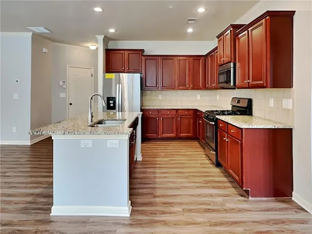 a kitchen with stainless steel appliances granite countertop a stove a sink dishwasher and a refrigerator with wooden floor