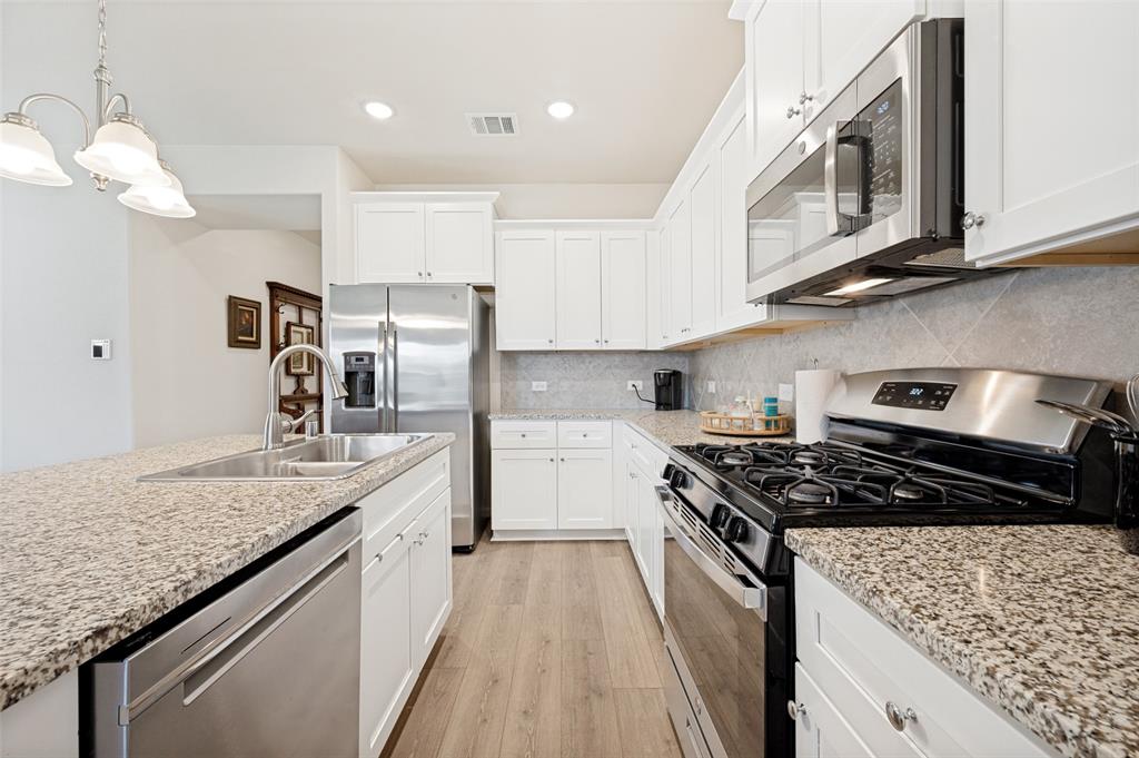 413 Wiggins Way Van Alstyne, TX 75495 - Photo 5 of 25 Kitchen featuring white cabinetry, light-toned granite countertops, stainless steel appliances, and wood-finish flooring
