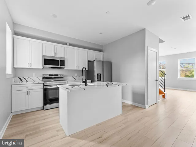 a kitchen with stainless steel appliances a stove top oven a sink a refrigerator white cabinets and wooden floor