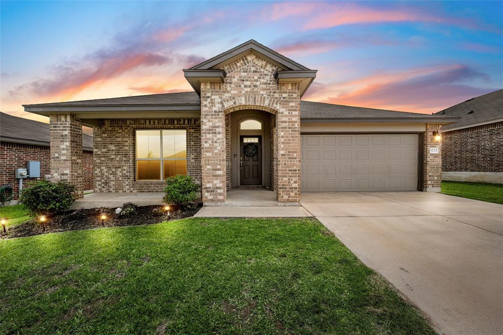 French country style house with brick siding, an attached garage, driveway, and a lawn