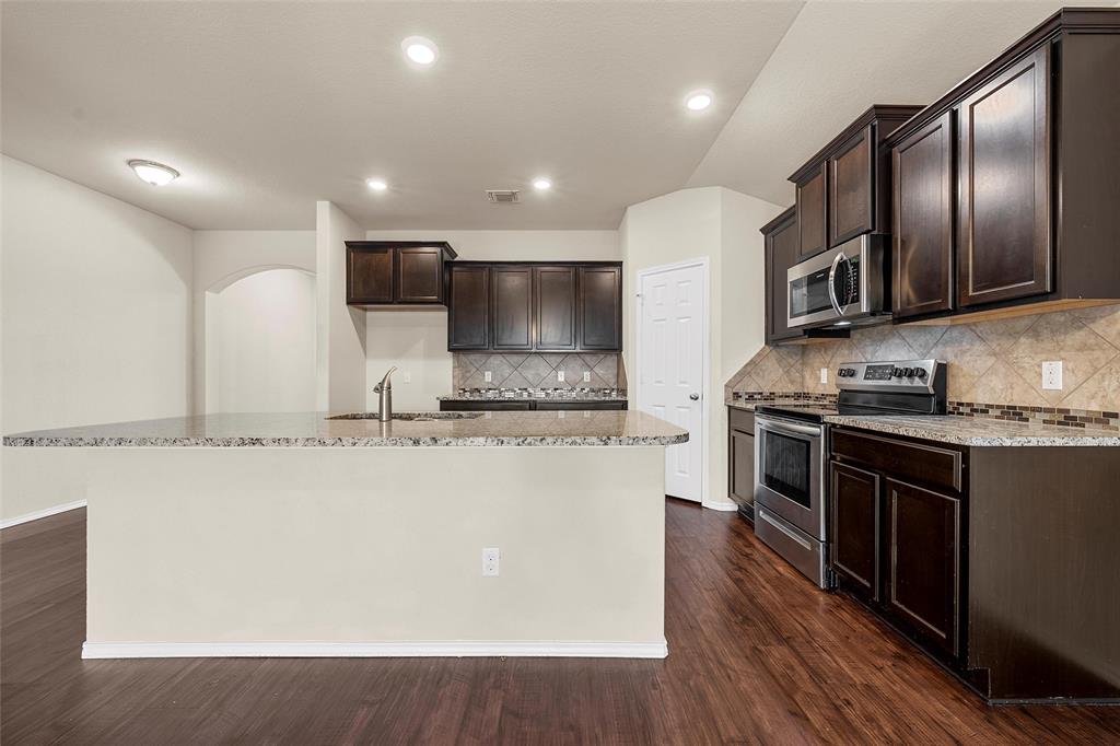 3217 Beutel Road Lorena, TX 76655 - Photo 13 of 40 Kitchen with appliances with stainless steel finishes, light stone counters, dark brown cabinets, an island with sink, and dark wood-style floors
