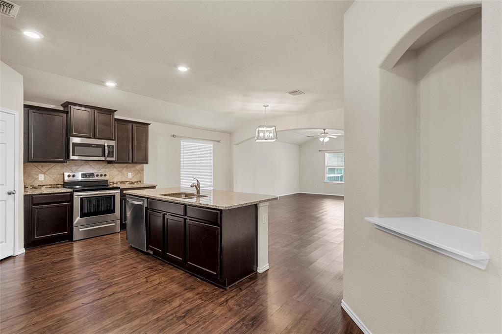 3217 Beutel Road Lorena, TX 76655 - Photo 9 of 40 Kitchen with appliances with stainless steel finishes, dark wood-style flooring, decorative backsplash, dark brown cabinets, and light stone countertops