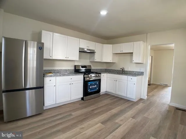 a kitchen with granite countertop a refrigerator oven a sink dishwasher and white cabinets with wooden floor