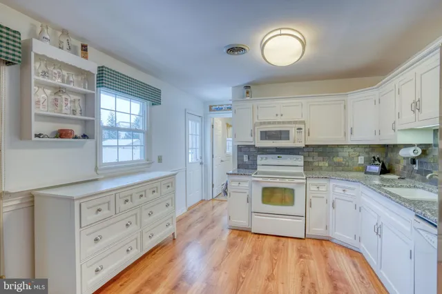 a kitchen with stainless steel appliances granite countertop a stove a sink dishwasher and white cabinets with wooden floor