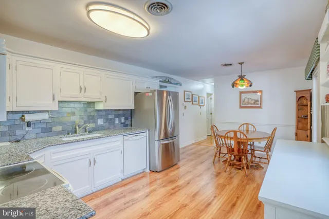 a kitchen with stainless steel appliances granite countertop a dining table chairs refrigerator and sink