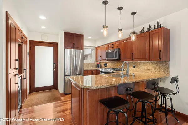 a kitchen with stainless steel appliances granite countertop a sink a stove a refrigerator and island with wooden floor