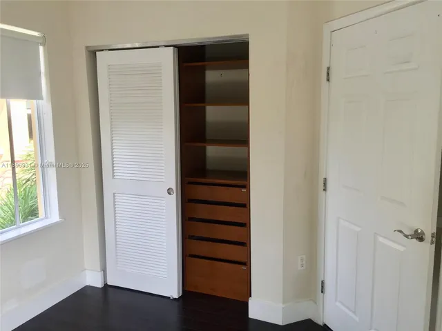 an empty room with wooden floor closet and windows