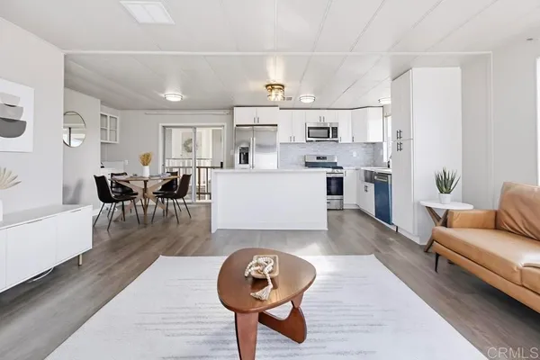 a living room with stainless steel appliances furniture a rug kitchen view and a chandelier