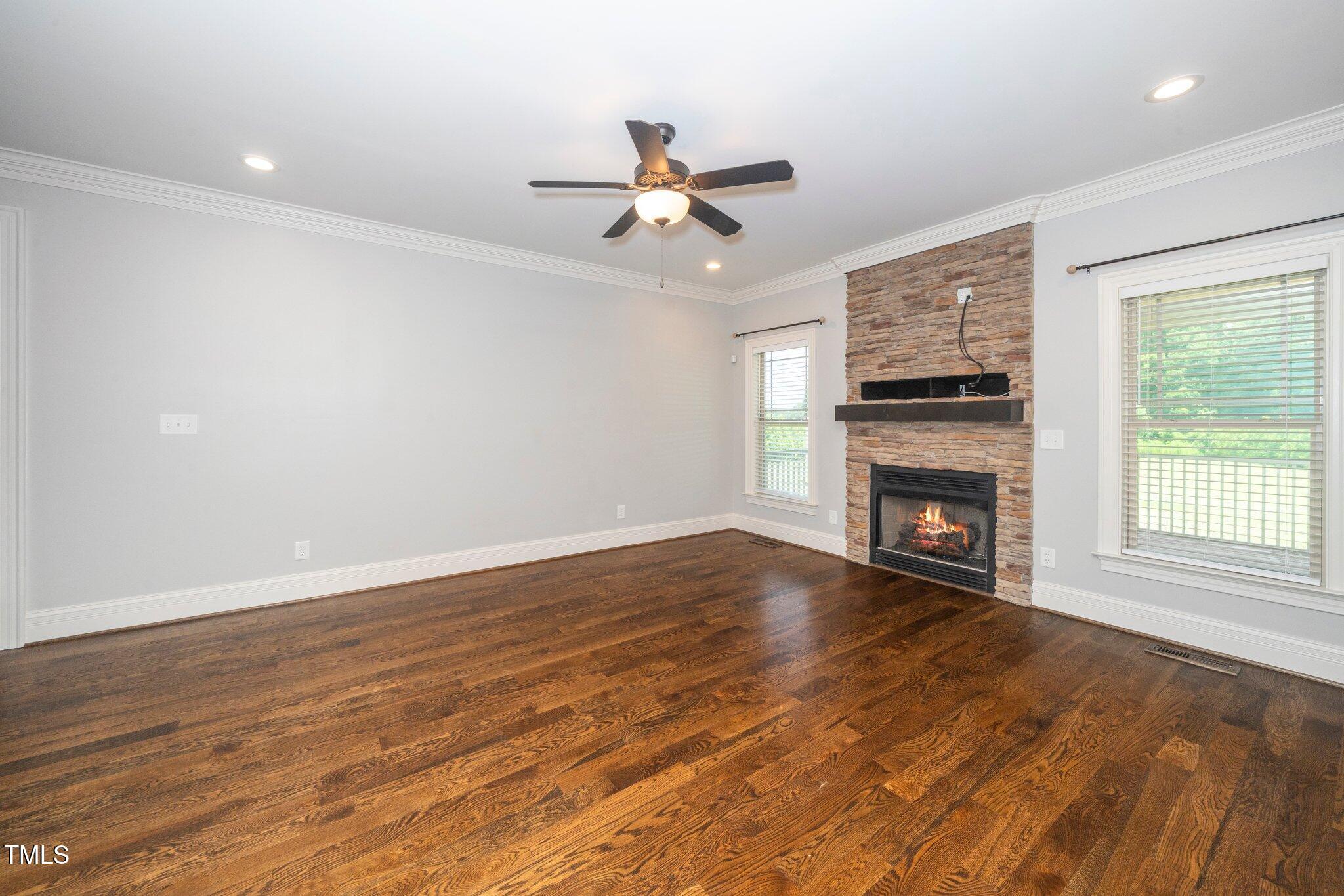 6737 Dwight Rowland Road Willow Spring, NC 27592 - Photo 11 of 50 an empty room with wooden floor a ceiling fan a fireplace and windows