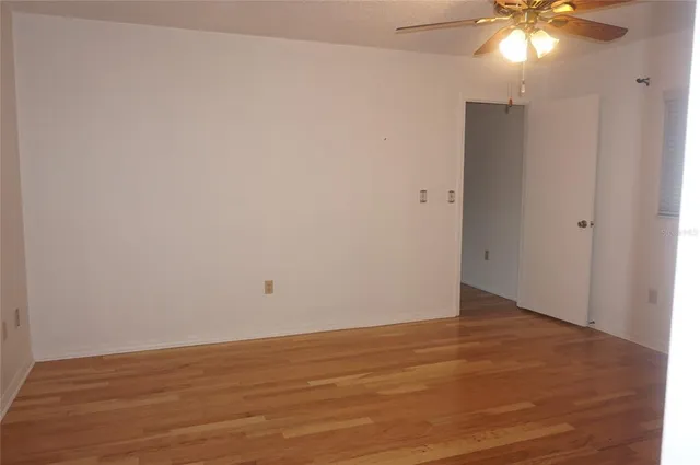 a view of an empty room with wooden floor and a chandelier fan