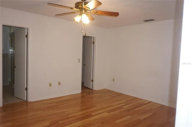 an empty room with wooden floor closet and fan