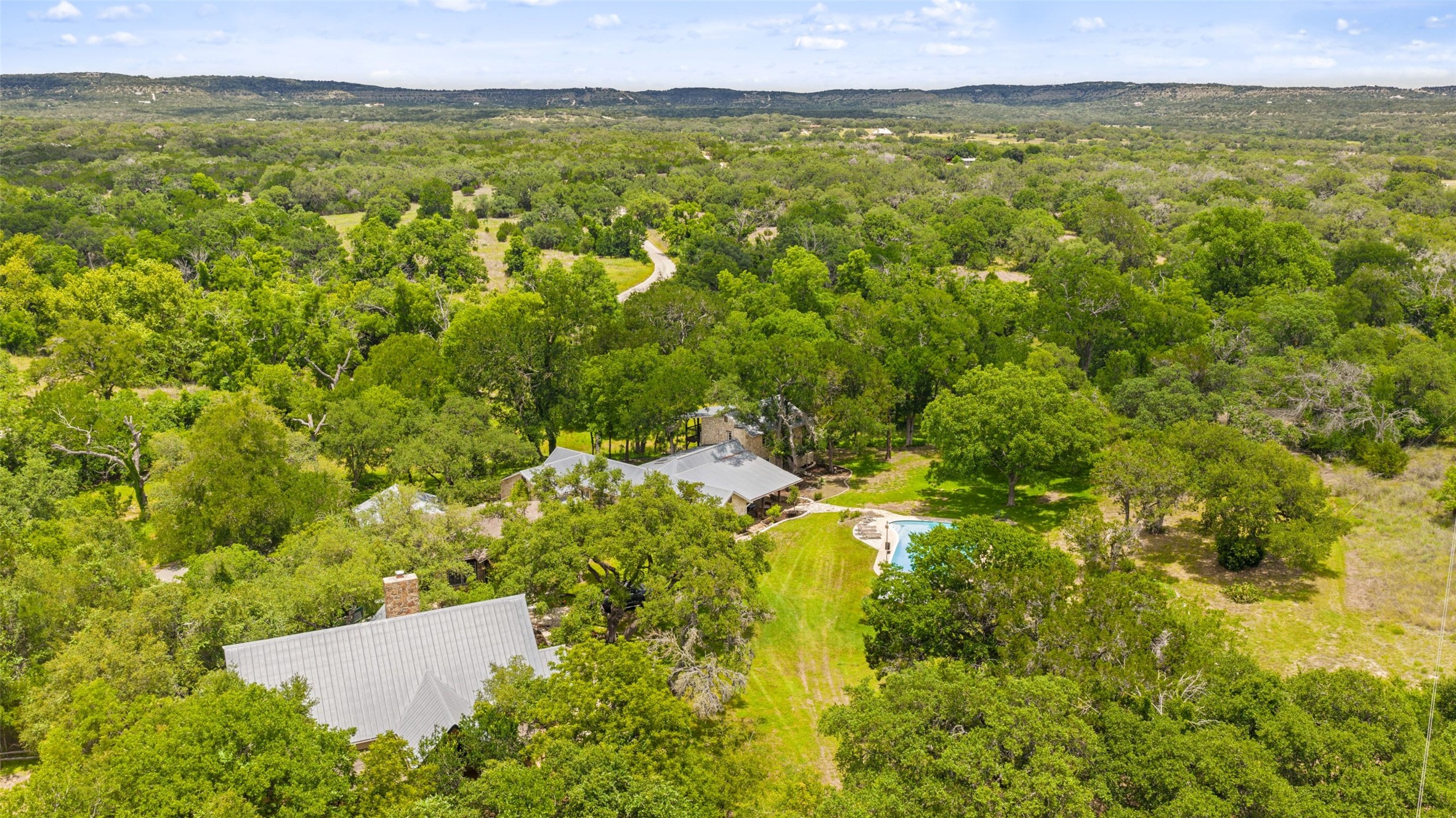 505 Red Corral Ranch Road Wimberley, TX 78676 - Photo 4 of 40 An aerial panorama reveals a private estate nestled within verdant woodlands, complete with a sparkling pool.