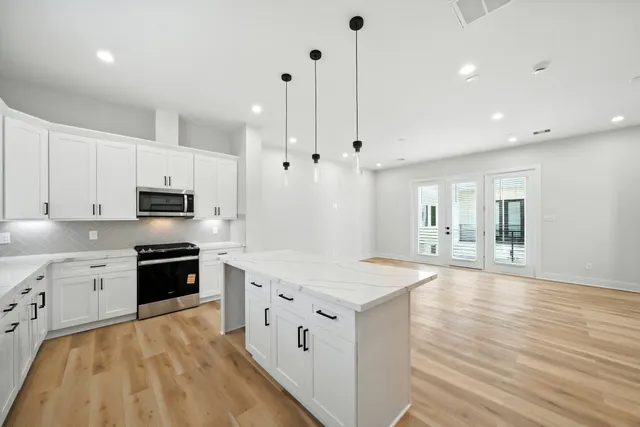 a large kitchen with stainless steel appliances a sink dishwasher a stove a refrigerator and white cabinets with wooden floor