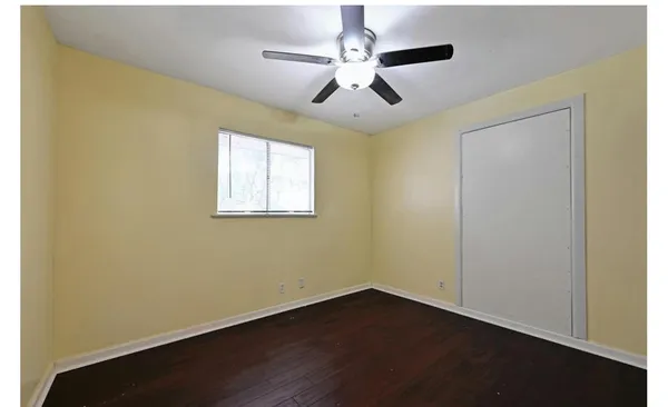 an empty room with wooden floor ceiling fan and windows