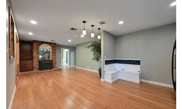 a view of an empty room with wooden floor and a kitchen