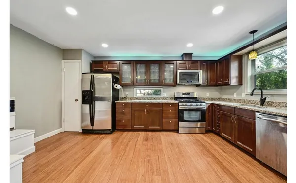 a kitchen with stainless steel appliances granite countertop wooden cabinets a refrigerator a sink a stove a microwave and wooden floors