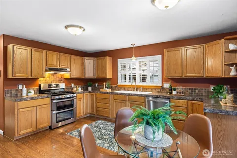 a kitchen with stainless steel appliances granite countertop a stove top oven a sink dishwasher a dining table and chairs with wooden floor