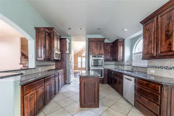 a kitchen with stainless steel appliances granite countertop wooden cabinets a sink dishwasher a stove and a refrigerator
