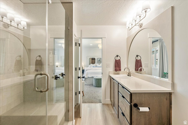 3916 South Sage Wood Avenue Mapleton, UT 84664 - Photo 18 of 33 Bathroom featuring a glass-enclosed shower with a built-in bench, a wood-finish vanity with a single sink and light-toned countertop, a large arched mirror, and wood-finish flooring