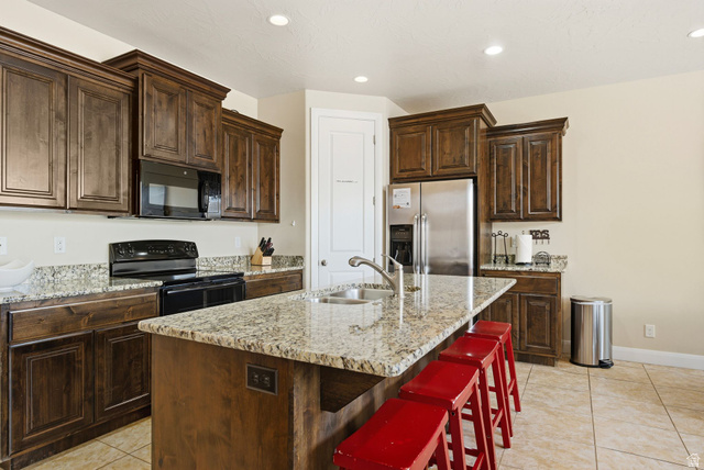 4269 Razor Drive Washington, UT 84780 - Photo 35 of 50 Kitchen with dark brown cabinets, black appliances, a kitchen breakfast bar, a center island with sink, and light stone counters