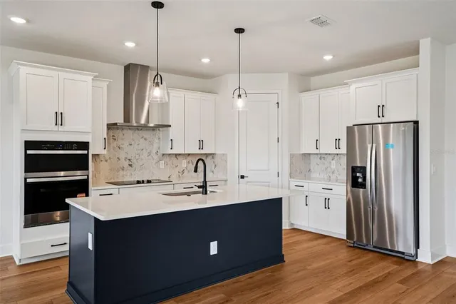 a kitchen with stainless steel appliances kitchen island granite countertop a refrigerator a sink dishwasher a oven and a view of wooden floor