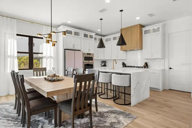 a kitchen with stainless steel appliances a stove a sink a dining table and chairs with wooden floor