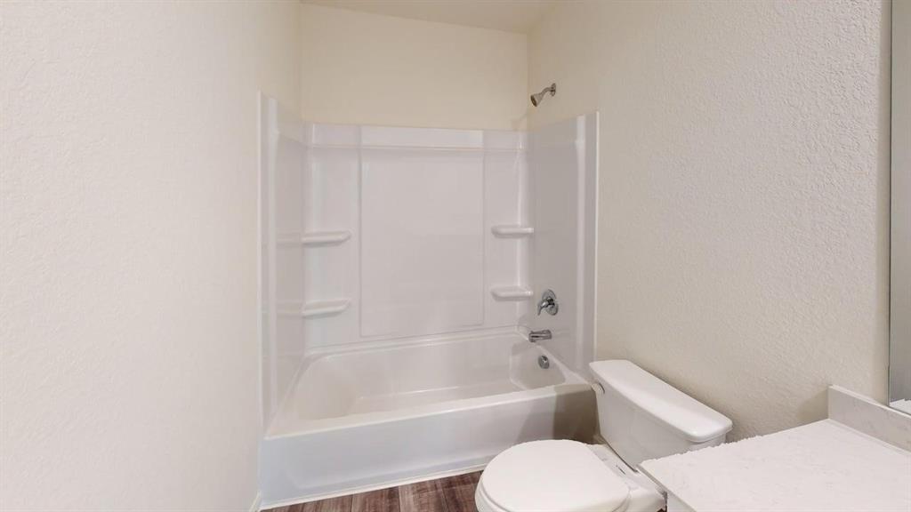 4529 Winecup Road Melissa, TX 75454 - Photo 22 of 29 Full bathroom featuring a white tub and shower combination with chrome fixtures, a white toilet, and wood-finish flooring