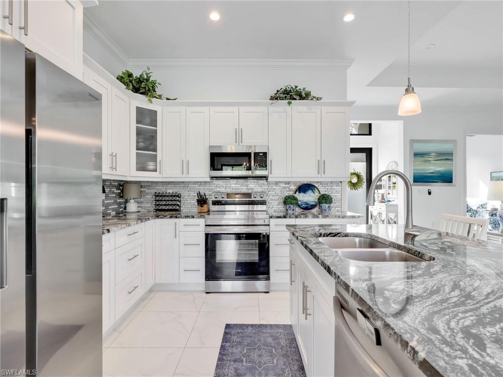 2007 22nd Avenue Northeast Naples, FL 34120 - Photo 11 of 47 Kitchen With White Shaker Cabinetry, Island, Pendant Lighting, Glass Tile Backsplash, Stainless-Steel Appliances, and Quartz Counters