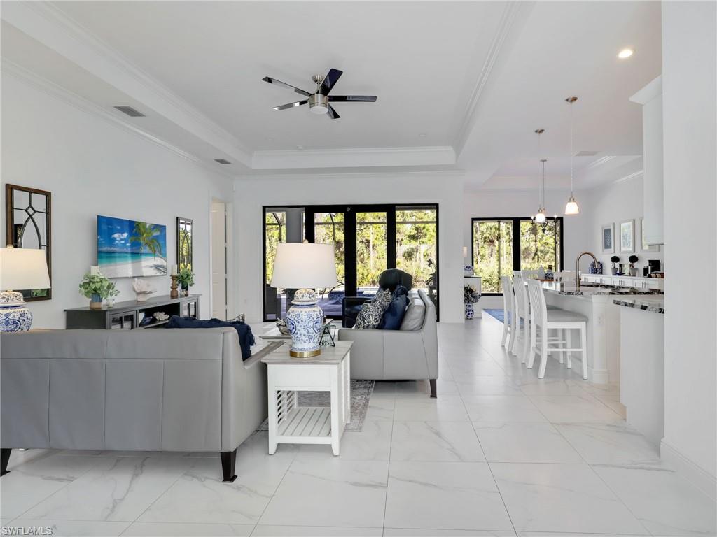 2007 22nd Avenue Northeast Naples, FL 34120 - Photo 30 of 47 Living Room With Tray Ceiling & Ceiling Fan, Kitchen With White Shaker Cabinetry, Island , Stainless-Steel Appliances, Quartz Counters, & Pool & Wooded Rear Yard View