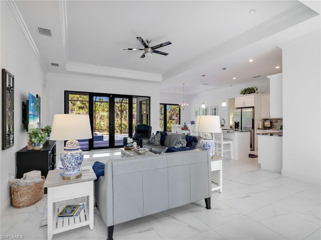 2007 22nd Avenue Northeast Naples, FL 34120 - Photo 6 of 47 Living Room with Tray Ceiling & Ceiling Fan, Kitchen With Island, White Shaker Cabinetry, Quartz Counters, & Dining Room, & Pool & Wooded Rear Yard Views