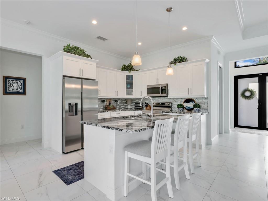 2007 22nd Avenue Northeast Naples, FL 34120 - Photo 7 of 47 Kitchen With White Shaker Cabinetry, Island, Glass Tile Backsplash, Stainless-Steel Appliances, & Quartz Counters