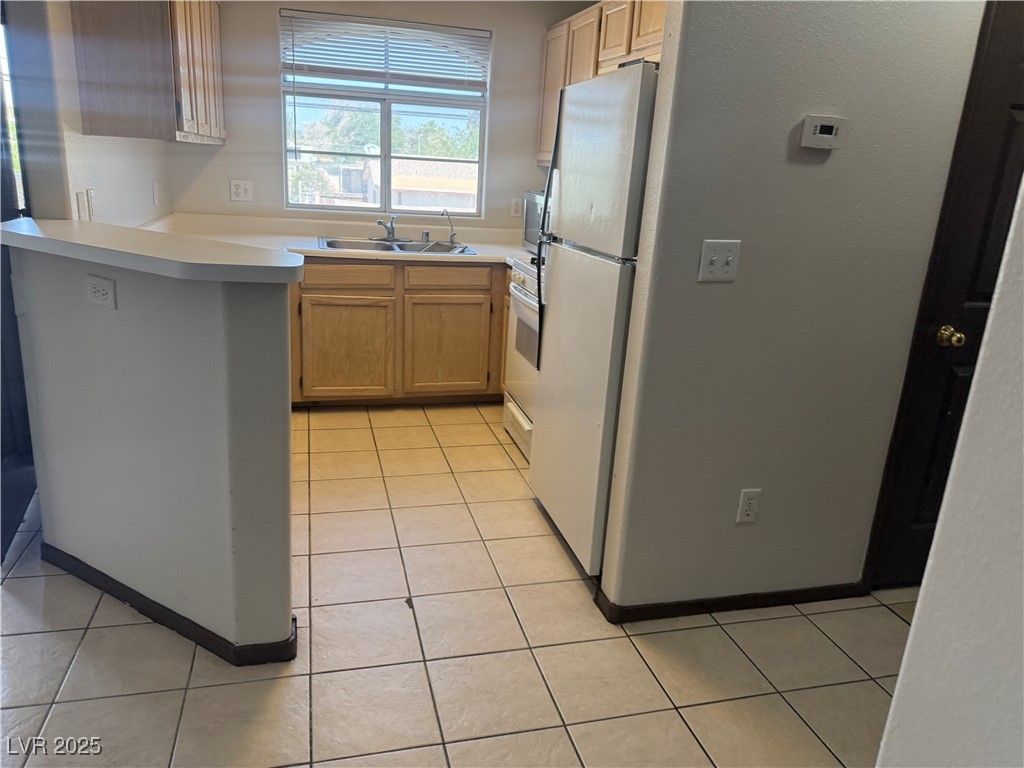 4500 West Lake Mead Boulevard, Unit 202 Las Vegas, NV 89108 - Photo 14 of 19 Kitchen with light countertops, white appliances, light tile patterned flooring, a peninsula, and light brown cabinets