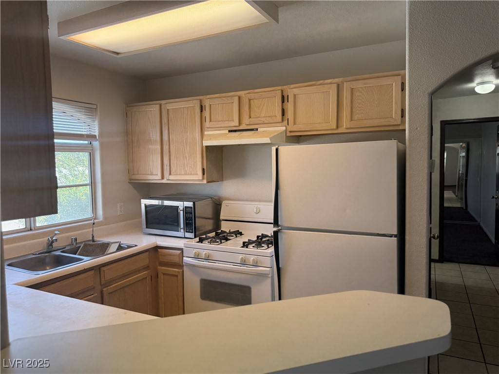 4500 West Lake Mead Boulevard, Unit 202 Las Vegas, NV 89108 - Photo 15 of 19 Kitchen with white appliances, light countertops, light brown cabinetry, and under cabinet range hood