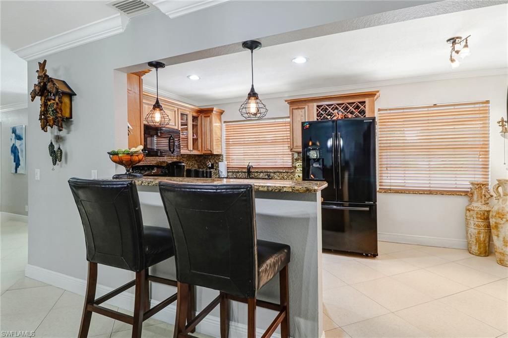 2329 41st Terrace Southwest Naples, FL 34116 - Photo 9 of 33 a kitchen with stainless steel appliances granite countertop a dining table chairs refrigerator and sink