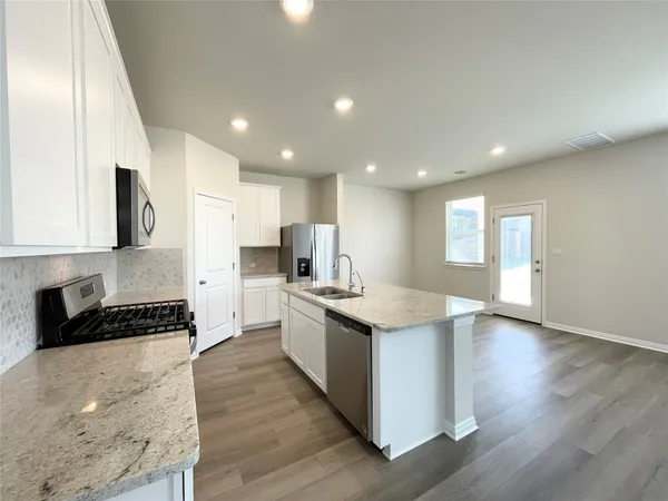 a kitchen with stainless steel appliances kitchen island granite countertop a stove a sink a refrigerator and white cabinets with wooden floor