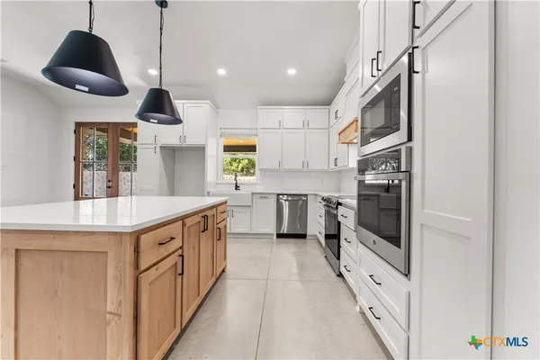 a kitchen with stainless steel appliances kitchen island a table chairs sink and cabinets