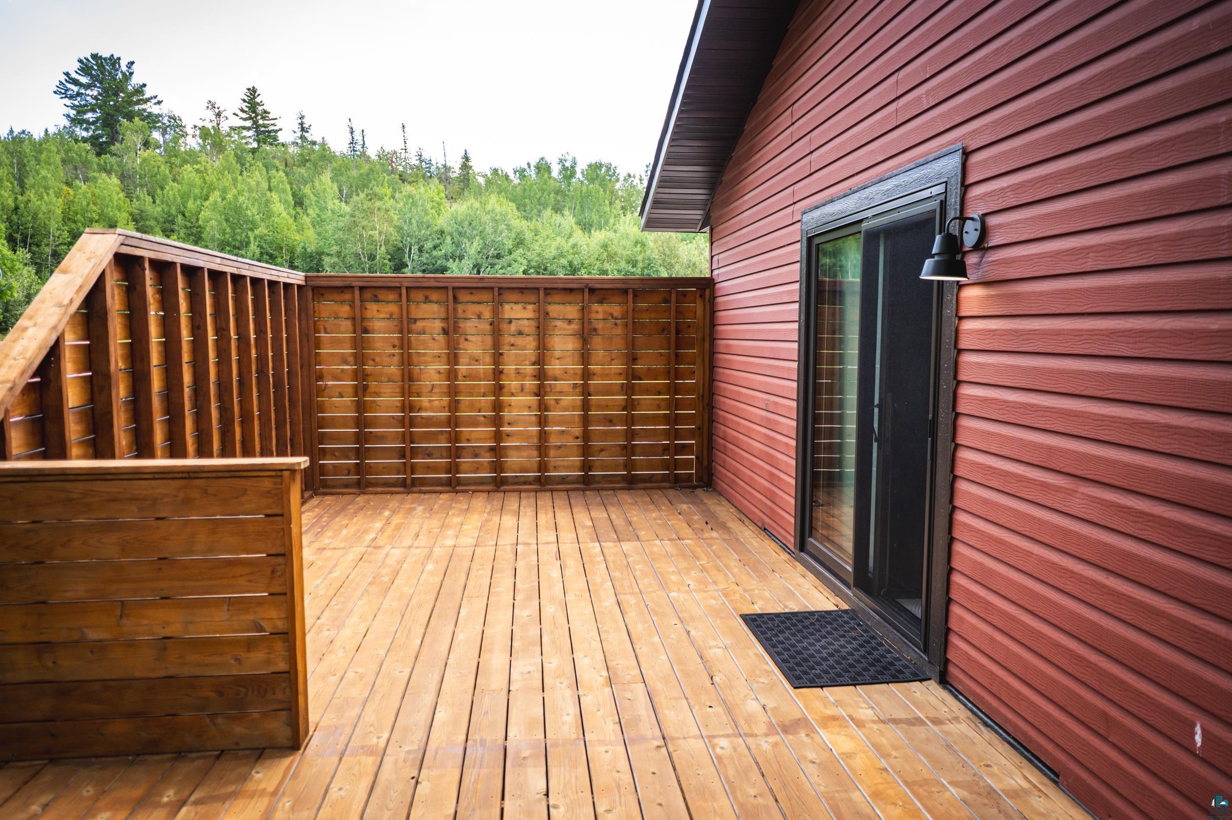 14635 Canadian Border Road Ely, MN 55731 - Photo 74 of 94 Spacious exterior deck with wood flooring, wood privacy fencing, red horizontal siding, and a black exterior light fixture