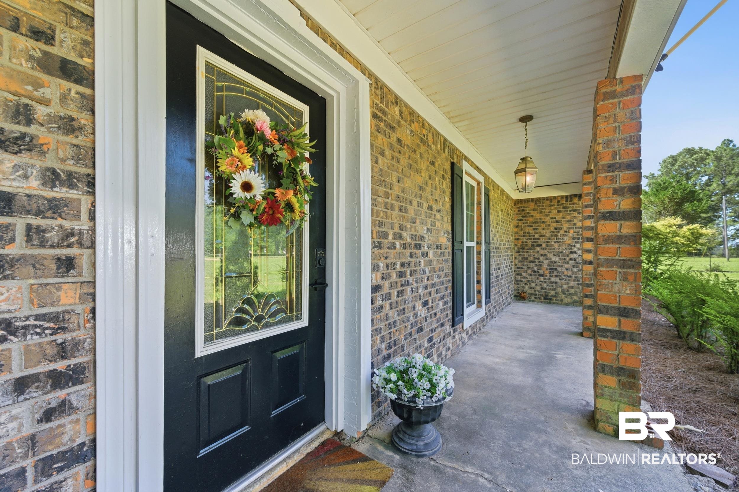 51620 Robert White Road Bay Minette, AL 36507 - Photo 9 of 81 Brick exterior with a covered porch featuring a black front door with decorative glass inserts, white trim, and dark window shutters